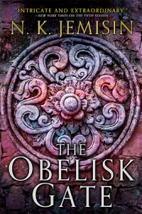 Cover of "The Obelisk Gate," featuring a floral design carved into stone and colored in swatches of pink, purple, and gray.