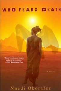 Cover of the book, featuring a Black person with medium-dark skin and long braids tied up in a messy knot. They are standing in an orange and red desert facing the sun and mountains in the distance. Wings like from a large bird are superimposed on the image, almost as if ghostly wings are sprouting from their back.