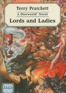 Cover of the book, featuring a shirtless man with goat legs and horns like tree branches reclining against an indistinct swirl of red and brown colors; in front of him, seen from behind, is a woman with a pointy black hat holding a torch.